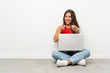 © luismolinero - Young woman with a laptop sitting on the floor points finger at you