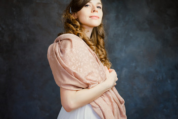 Pretty romantic girl with curly brown hair standing over dark wall. Natural makeup. Feminine elegant caucasian young woman.