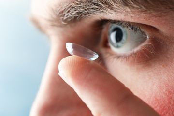 Inserting a corrective contact lens. Man with blue eyes