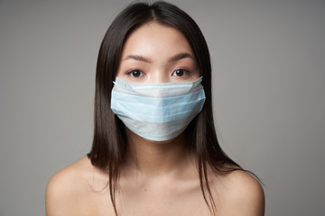  A young beautiful Asian woman in a medical mask, on an isolated gray background, looks directly at the camera. Concept of health,protection, prevention of bacterial infection