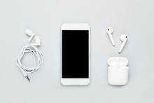 White Wireless Earbuds With Earphones And Mobile Phone On Grey Background
