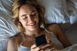 © PhotoAlto - Close-up of smiling young woman using smartphone while lying on bed in bedroom