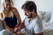 © PhotoAlto - Smiling young couple using smartphone while sitting on bed in bedroom
