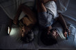 © PhotoAlto - Young couple using their smartphones while lying back to back on bed at night
