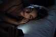 © PhotoAlto - Young woman using smartphone while lying on bed in bedroom at night