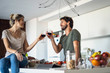© PhotoAlto - Smiling couple toasting wine glasses in kitchen while standing in kitchen