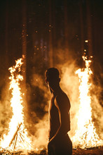 Man Standing Between And In Front Of 2 Large Bonfires