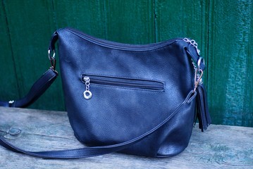 one black closed leather bag stands on a gray wooden table against a green wall