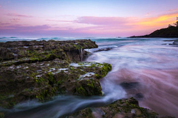 Tranquil Long Exposure of Smooth Ocean Water Coming over Rocks on Sandy Beach with Colorful Pastel Sunrise Sky at Dawn on Maui Hawaii in Relaxing Tropical Island Paradise 