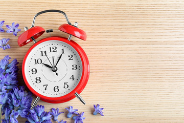 Poster - Red alarm clock, spring flowers and space for text on wooden table, flat lay. Time change