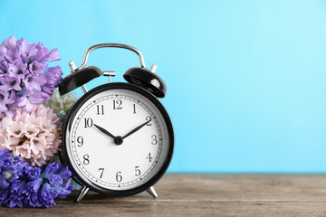 Poster - Black alarm clock and spring flowers on light blue background, space for text. Time change