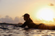© Cavan Images - Female surfer lying on surfboard in the evening