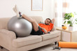 Lazy young man with sport equipment on sofa at home