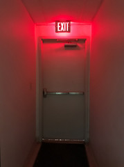 emergency exit door at the end of the hall with the exit light on.
