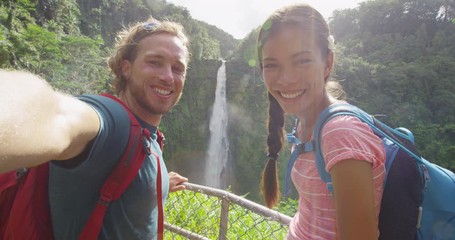 Wall Mural - Hawaii couple tourists taking travel phone selfie self portrait with camera phone on Hawaii, Big Islands, Akaka Falls. Happy cheerful young multicultural couple on travel.