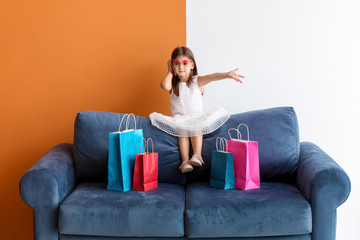 Sticker - Stylish little girl with shopping bags talking by phone while sitting on sofa