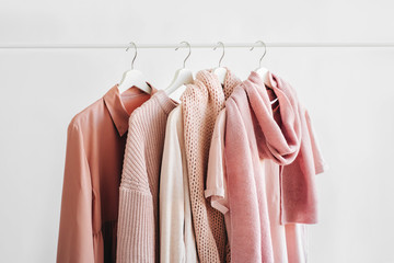 Feminine clothes in pastel pink color on hanger on white background. Spring cleaning home wardrobe. Minimal fashion concept.