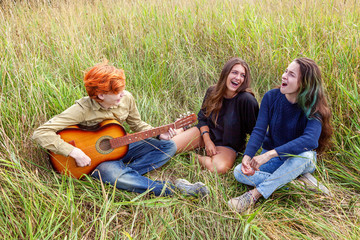 Summer holidays vacation music happy people concept. Group of three friends boy and two girls with guitar singing song having fun together outdoors. Picnic with friends on road trip in nature.