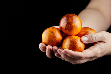 Hanful of whole red oranges on black background