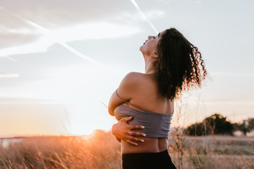 black girl hugging herself with the sky and the beach in the background