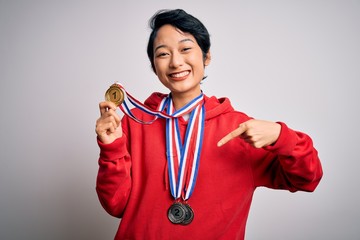 Canvas Print - Young beautiful asian girl winner wearing medals over isolated white background with surprise face pointing finger to himself