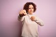 © Krakenimages.com - Middle age beautiful curly hair woman wearing casual turtleneck sweater over pink background Punching fist to fight, aggressive and angry attack, threat and violence