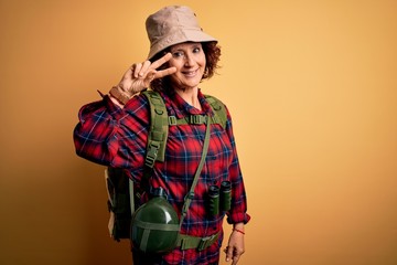 Sticker - Middle age curly hair hiker woman hiking wearing backpack and water canteen using binoculars Doing peace symbol with fingers over face, smiling cheerful showing victory