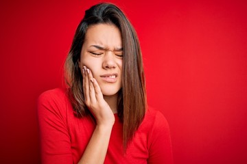 Wall Mural - Young beautiful brunette girl wearing casual t-shirt over isolated red background touching mouth with hand with painful expression because of toothache or dental illness on teeth. Dentist concept.