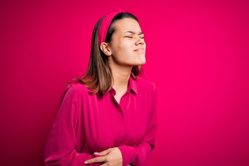 Wall Mural - Young beautiful brunette girl wearing casual shirt standing over isolated pink background with hand on stomach because nausea, painful disease feeling unwell. Ache concept.