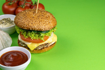 Wall Mural - Hamburgers close-up on a green background, nearby are french fries, sauces and tomatoes, as well as salted and peppercorn