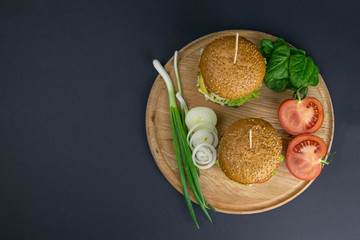 Wall Mural - Two hamburgers close-up on a round wooden board, next to, tomatoes, chopped onions and spinach leaves