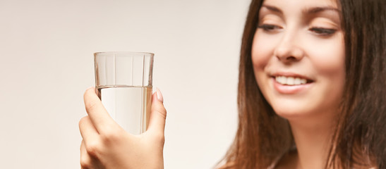 Pretty girl hold pure water glass. Smiling face. Health lifestyle. Clear beverage. Natural transparent nutrition. Teeth background. Young woman hand. Female person at studio. Horizontal banner