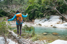 A Woman With A Backpack Crosses A River On A Log.
