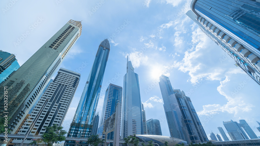Looking up to high-rise office buildings, skyscrapers, architectures in financial district with blue sky. Smart urban city for business and technology concept background in Downtown Dubai, UAE. - obrazy, fototapety, plakaty 