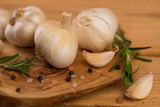 Fototapeta Miasto - Fresh garlic with spices on a wooden background, thyme and rosemary. Culinary background, ingredients for marinade, closeup