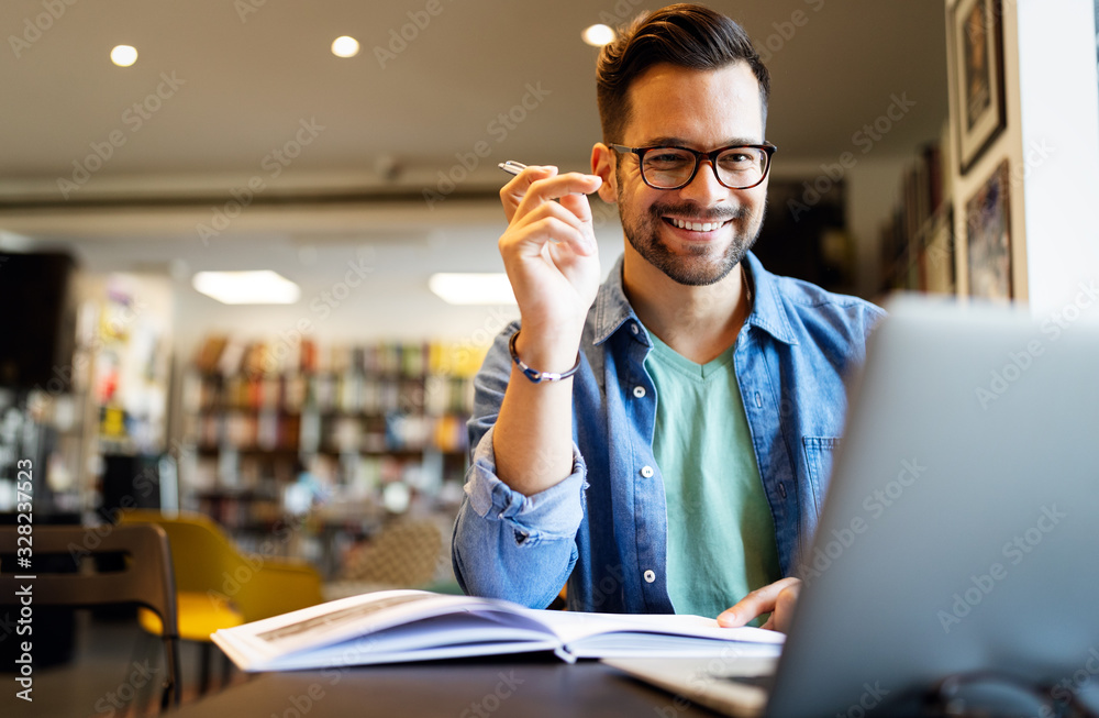 Smiling male student working and studying in a library - obrazy, fototapety, plakaty 