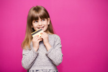Joyful Little Blonde Shy Face Girl 6-7 Years Old Hold Credit Bank Card Isolated On Pink. Childhood Lifestyle Concept.