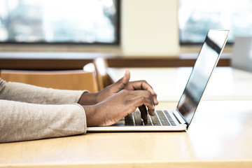 Wall Mural - Female black student working on computer in classroom. Hands of young woman sitting at desk and using laptop in classroom. Wireless technology concept