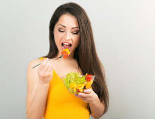 Beautiful smiling positive woman eating healthy organic vegatable salad in yellow bright clothing on blue background. Closeup