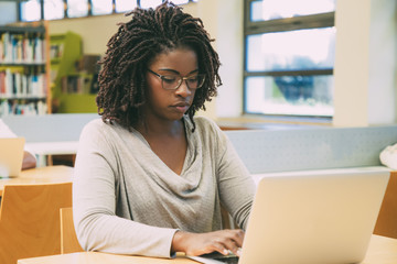 Wall Mural - focused student working in library computer class. young black woman sitting at desk and using lapto