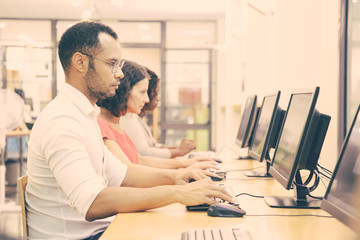 Wall Mural - diverse group of students taking online tests in computer class. line of man and women in casual sit