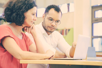 Wall Mural - two adult students working on class presentation in library. man and woman in casual sitting at desk