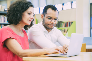 Wall Mural - two adult students collecting data for presentation in library. man and woman in casual sitting at d