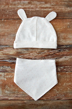Babyhood And Clothing Concept - White Baby Hat With Ears And Bib On Wooden Table