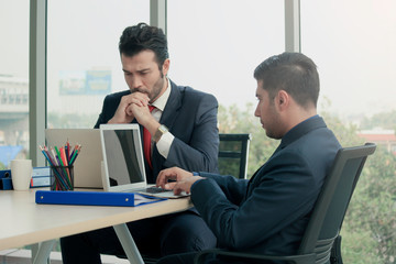 Two young businessmen using laptop computer seriously discussing about project work and communicating while sitting at the office desk together at conference meeting, businesspeople talking on meeting