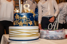 18 Birthday Party. Gold And Blue Fondant Birthday Cake With Number 18 On The Top Over The Party Blurred Background.