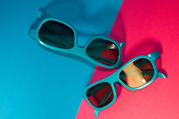 On bright pink background lie sunglasses in plastic blue frame with dark glasses. Summer. Accessories.