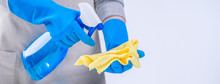 Young Woman Housekeeper Is Doing Cleaning White Table In Apron With Blue Gloves, Spray Cleaner, Wet Yellow Rag, Close Up, Copy Space, Blank Design Concept.