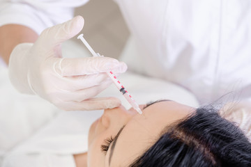 Wall Mural - Beauty procedure. Portrait young woman receiving hyaluronic acid injection in a forehead. Painful procedure on female face. Lifting skin treatment