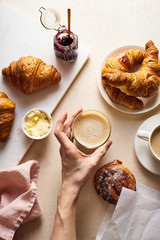 Wall Mural - Flatlay with coffee and croissants. Female hand holding a cup of capuccino. Breakfast beverage with pastry. Morning set